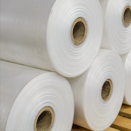 Rolls of white polyethylene film stacked on a wooden pallet, their kraft cores facing the camera.