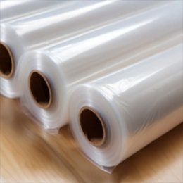 Three rolls of clear polyethylene bundling film standing on a wooden surface.